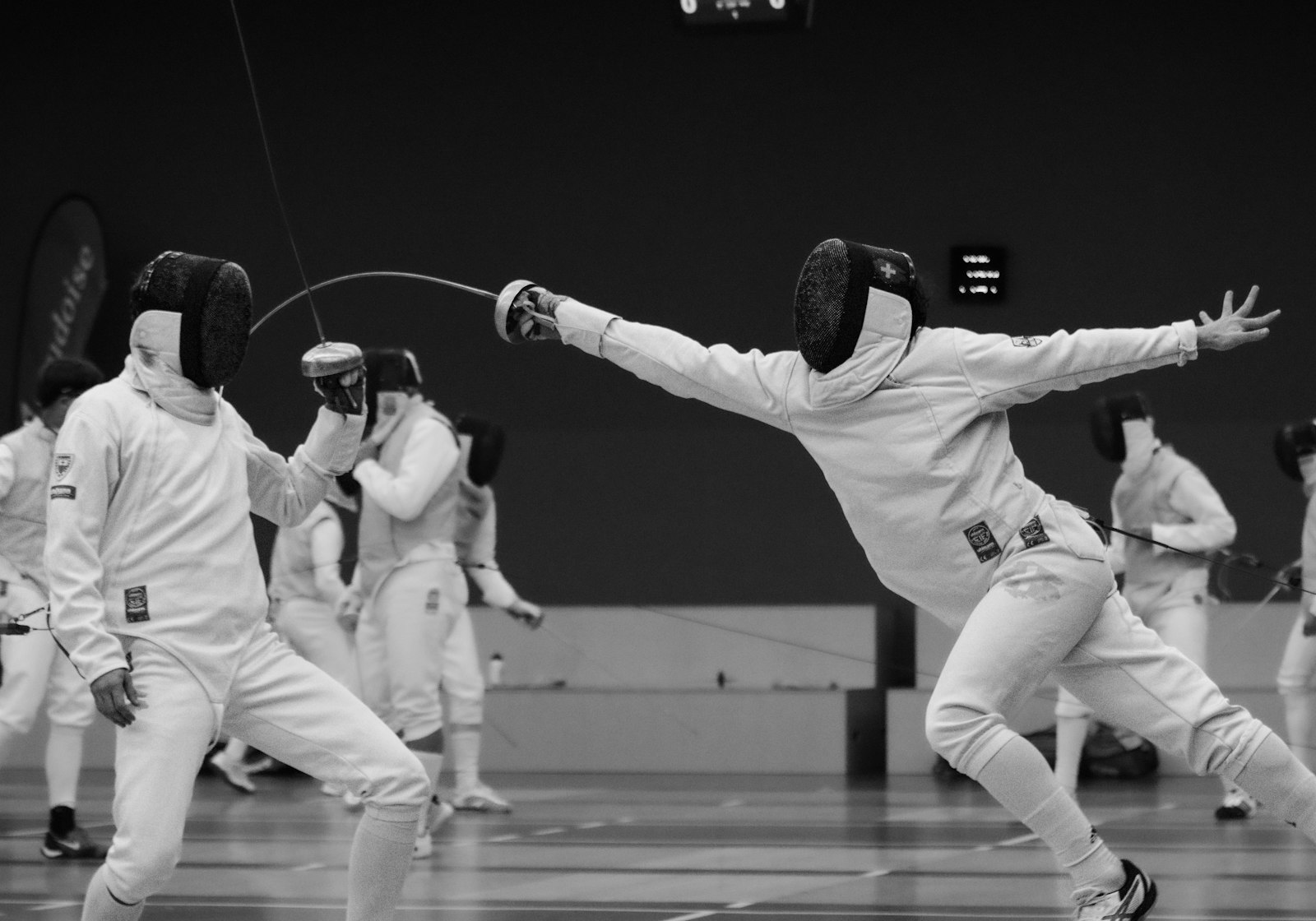 Two épée fencers in a bout in a sports hall, one stretched out in a full lunge