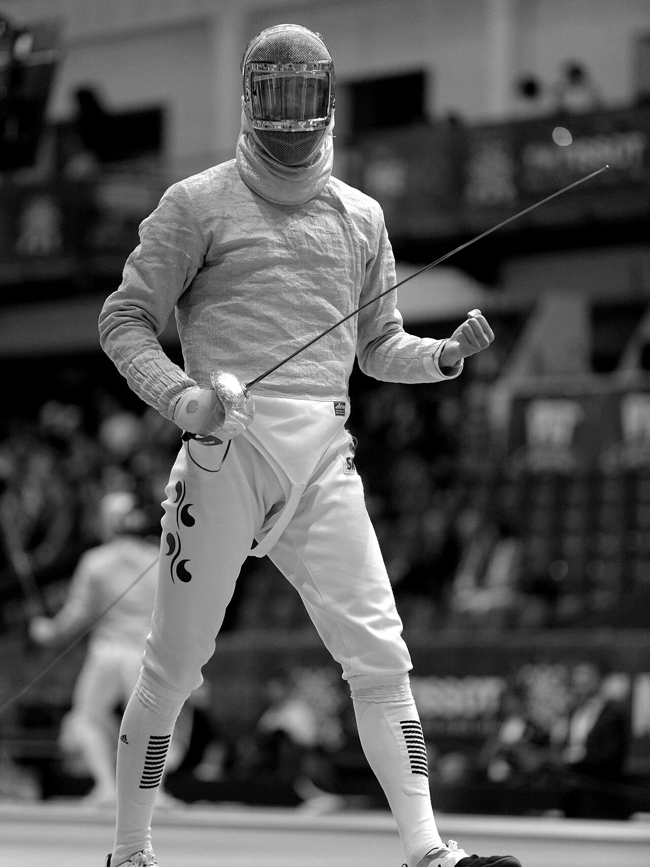 Sabre fencer in mask and white kit, holding a sabre, on the piste at a competition